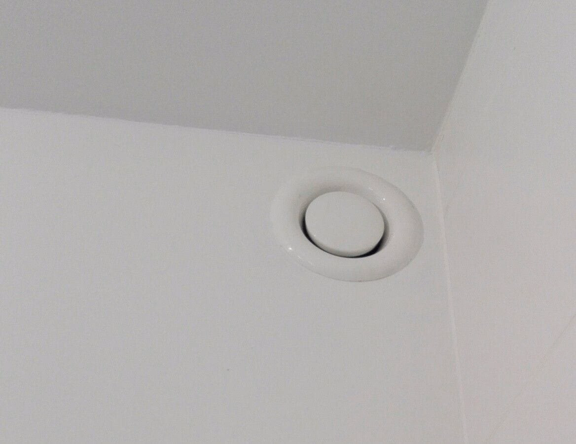 Ventilatieventiel bovenaan een witte muur, vlak onder het plafond